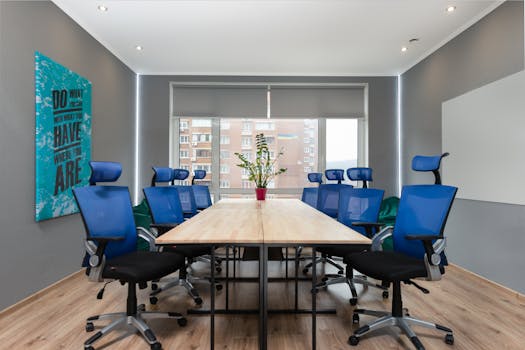 Armchairs at table with green plant placed near wall with creative signboard in modern conference room with window in office